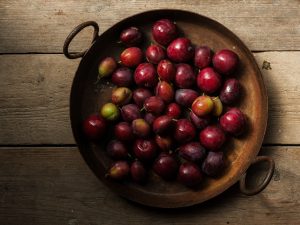Walled garden plums in a metal bowl on a wooden surface.