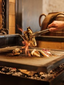 Raddichio being cooked over a wood-fire grill with flames coming up between the grill.
