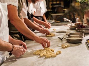 Chefs rolling out gnocchi using forks with piles of goncchi in front of them.