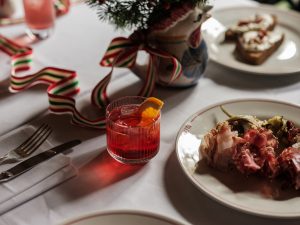 A plate of sharing charcuterie with a glass of negroni, cutlery and a chicken jug with seasonal greenery in the background.