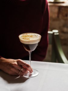 A espresso martini cocktail in a glass with a hand on the stem.