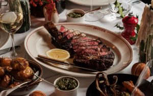 A sharing steak on a plate with sides and glasses of wine around it.