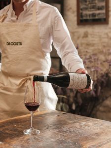 Red wine being poured into a glass by a person in a Da Costa cream apron.