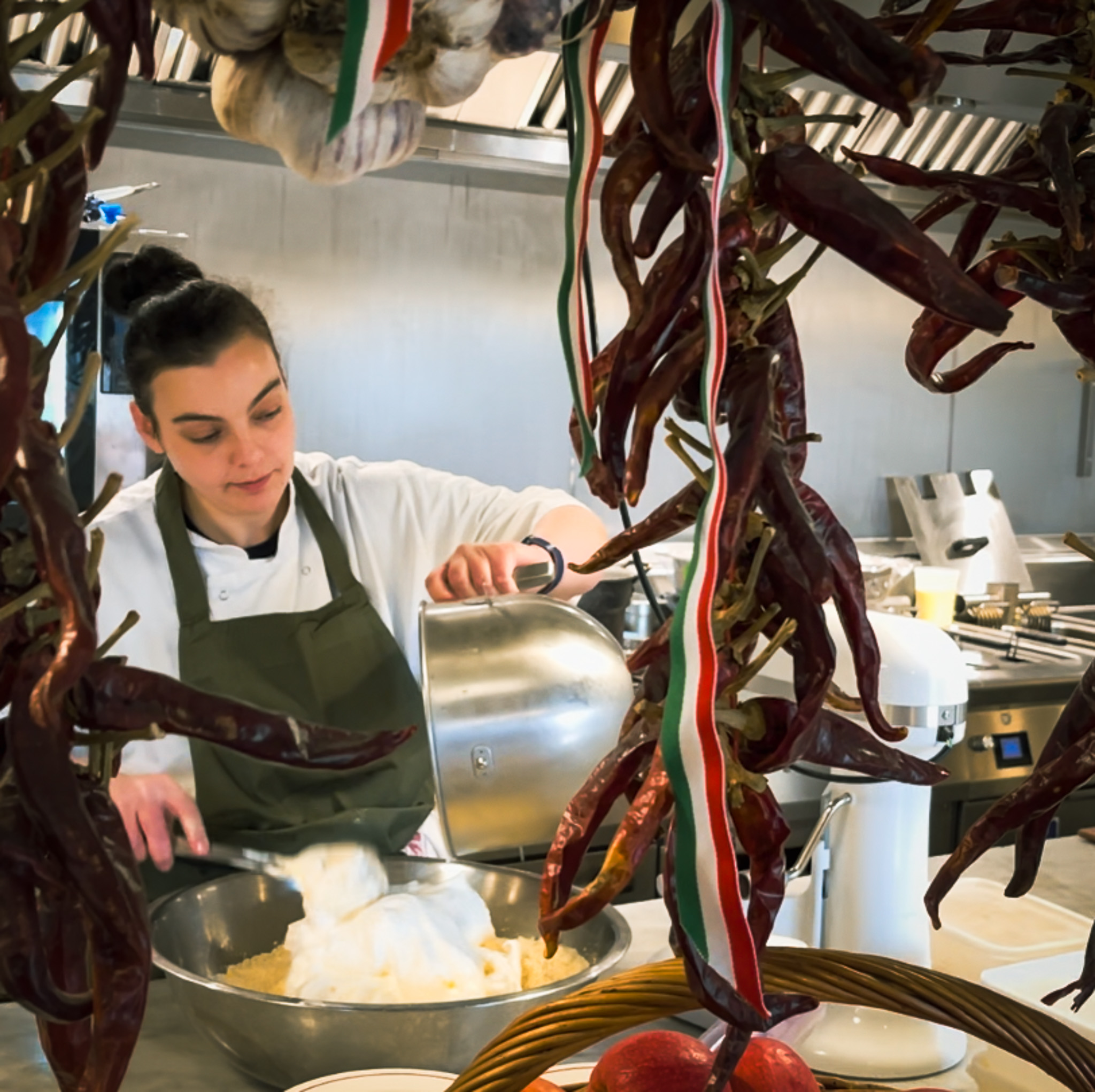A female chef pouring whipped egg whites into a mixing bowl, framed by chillies and ribbons.