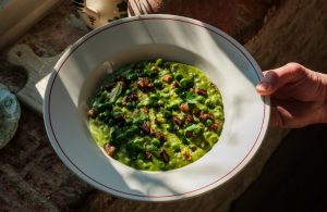 Risi e Bisi, a green pea and pancetta risotto in a bowl held by a a hand in the sunlight.