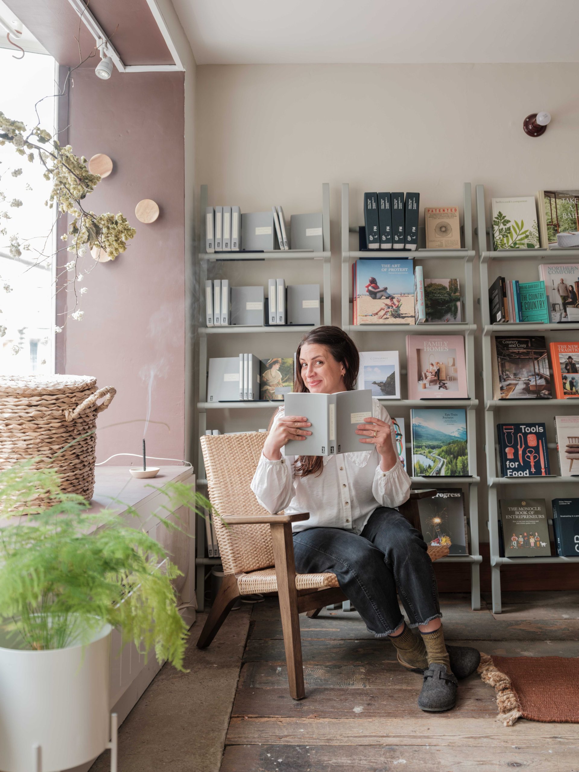 A women sitting in a chair in front of book shelves, holding a book.