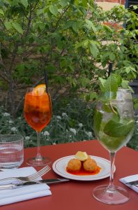 Two glasses of with different spritzes in on a table with arancini.