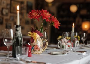 A close up of a table laid for dinner with a candle lit and a chicken jug with fresh flowers.