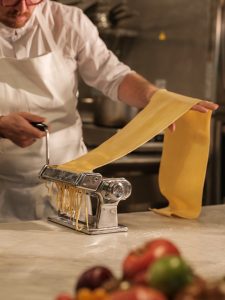 A person making bigoli pasta using a pasta machine.
