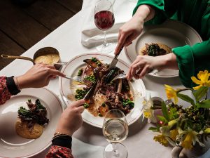People using cutlery to take portions of beef off a sharing joint and onto their plates.