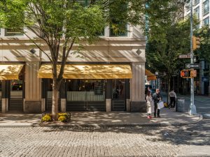 The front of a restaurant in the sunshine with a tree in front of it.