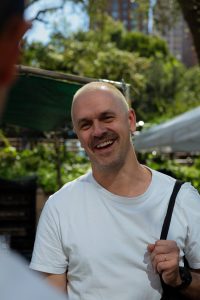 A man smiling in front of trees and buildings.