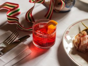 A glass of red liquid with a slice of orange on top of it.