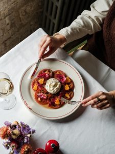 Woman sitting at a table eating burrata with winter tomatoes and basil.