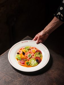 A hand holding a plate of a tomato salad