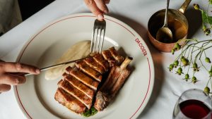 A pork chop sliced on a Da Costa branded plate with a knife and fork hovering above